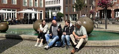 Foto von (v.l.) Eliza Diekmann-Cloppenburg, André Stinka, Matthis Tasler, Philipp Hänsel im Gespräch am Brunnen auf dem Marktplatz in Coesfeld.